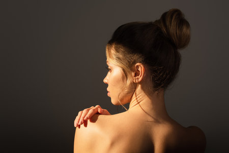back view of young woman with perfect skin touching naked shoulder isolated on greyの写真素材