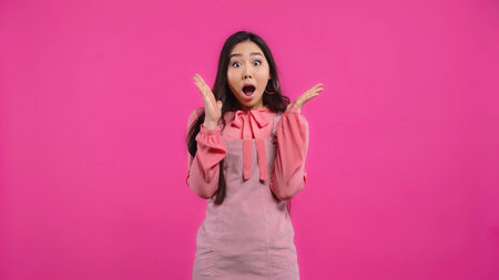 shocked asian woman with opened mouth gesturing isolated on pinkの写真素材