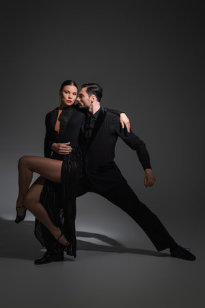 Dancer in suit hugging partner with red lips while performing tango on grey background with shadowの写真素材