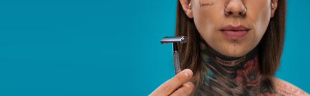 cropped view of young man with tattoos holding safety razor isolated on blueの写真素材