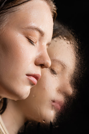 Close up view of young woman with wet skin posing near near mirror on black backgroundの写真素材