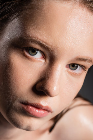 Close up view of woman with wet skin and hair looking at camera isolated on greyの写真素材