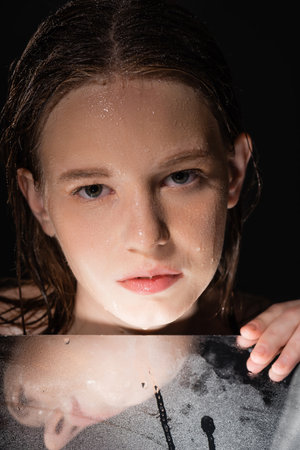 Portrait of model with wet face touching mirror isolated on blackの写真素材