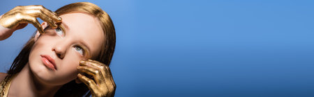 Portrait of young woman with golden dye on hands and hair touching face isolated on blue, banner
