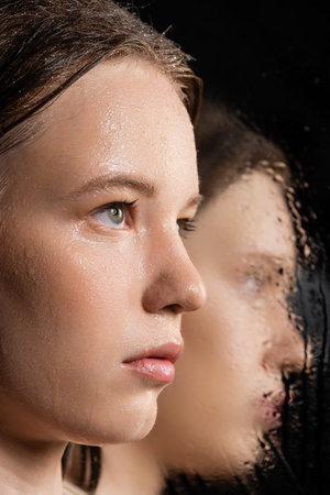 Close up view of fair haired woman with wet skin looking away near blurred mirror on blackの写真素材