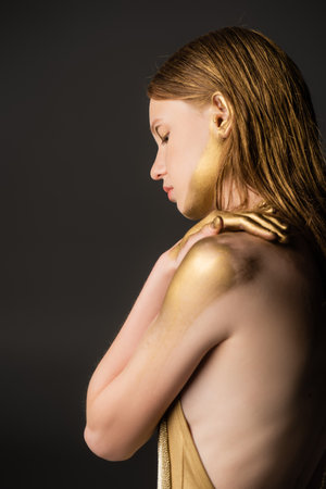 Side view of woman with makeup and golden paint on skin isolated on greyの写真素材