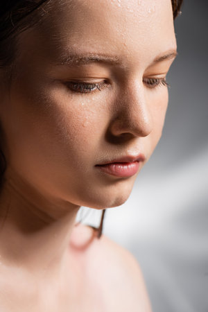 Young woman with water drops on face on abstract grey backgroundの写真素材