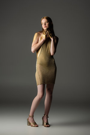 Full length of stylish young model in golden paint on skin standing on grey backgroundの写真素材