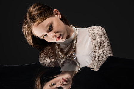 Fair haired model in knitted cardigan and pearl necklace looking at camera near reflective surface...