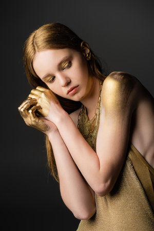 Young woman in golden paint and dress posing isolated on greyの写真素材