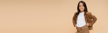 cheerful girl in stylish autumn jacket posing with hands on hips isolated on beige, bannerの写真素材