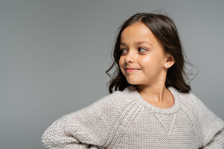 brunette girl in warm sweater smiling and looking away isolated on greyの写真素材