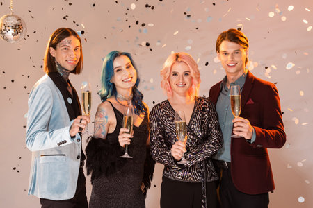 joyful nonbinary people with champagne glasses looking at camera while celebrating christmas on beige backgroundの写真素材