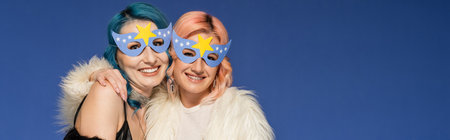 happy nonbinary friends in party masks hugging isolated on blue, bannerの写真素材