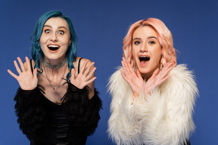 astonished nonbinary friends showing wow gesture and looking at camera isolated on blueの写真素材