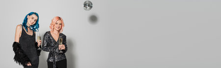 smiling nonbinary friends standing with champagne glasses near disco ball on grey background, bannerの写真素材