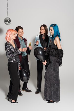 cheerful and elegant queer people with champagne glasses and black balloons on grey backgroundの写真素材