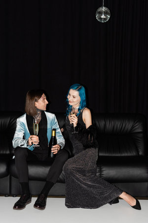 elegant queer friends holding champagne glasses while celebrating christmas on leather couch on black backgroundの写真素材