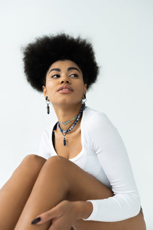 curly and young african american woman in long sleeve shirt isolated on white