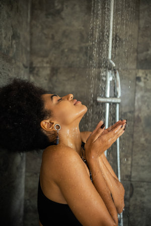 pleased african american woman with closed eyes taking shower at homeの写真素材