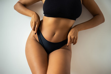 Cropped view of sexy african american woman in crop top touching black panties near wall at homeの写真素材