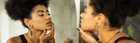 Side view of african american woman touching chin while looking at mirror at home, bannerの写真素材