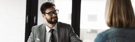 Positive businessman in formal wear looking at blurred woman during job interview in office, bannerの写真素材