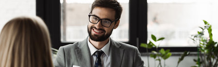 Cheerful businessman in suit looking at blurred woman on job interview in office, bannerの写真素材
