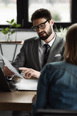Businessman pointing at resume while talking to blurred candidate on job interviewの写真素材