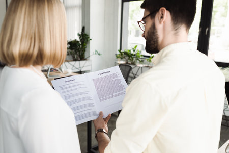 Businessman in eyeglasses holding contract near young intern in officeの写真素材