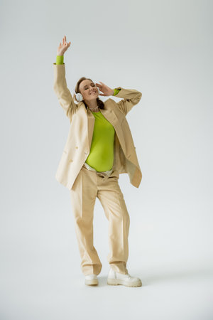 Full length of stylish pregnant woman listening music in headphones on grey backgroundの写真素材