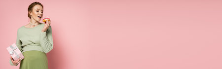 Pregnant woman with open mouth holding donut and gift box on pink background, banner
