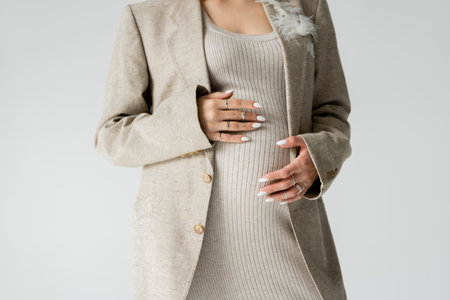 Cropped view of stylish pregnant woman in jacket touching belly isolated on greyの写真素材