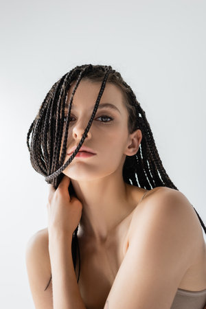 Portrait of young model with braids looking at camera isolated on grey