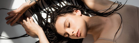 Top view of young woman in sports bra lying on grey background with light, banner