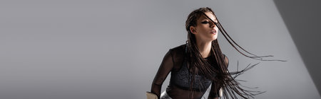 young futuristic woman with dreadlocks posing in black clothes on grey background, banner