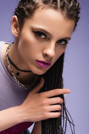 portrait of stylish woman in necklaces and makeup looking at camera isolated on purple