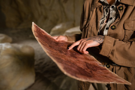 cropped view of archaeologist in brown jacket pointing at ancient map in cave
