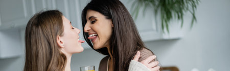 Young lesbian couple sticking out tongues in kitchen, bannerの写真素材
