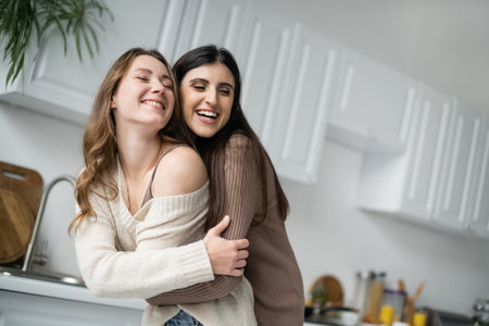 Cheerful lesbian woman hugging young girlfriend in kitchen