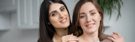 Same sex couple hugging and looking at camera at home, bannerの写真素材