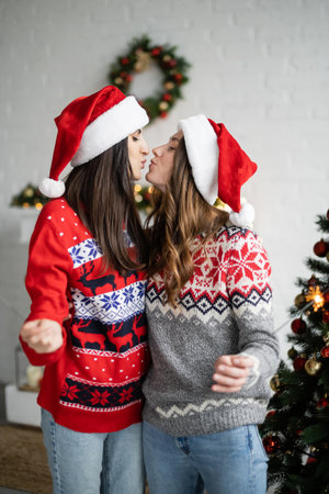 Side view of same sex couple in santa hats kissing and holding sparklers in living roomの写真素材