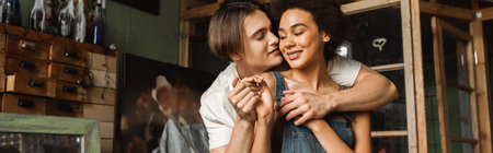 happy interracial couple holding hands end embracing in art studio, bannerの写真素材