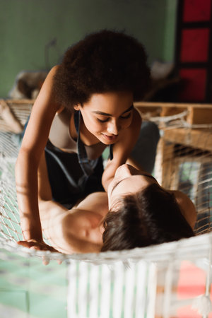 passionate african american woman looking at shirtless man lying in net hammock in workshopの写真素材