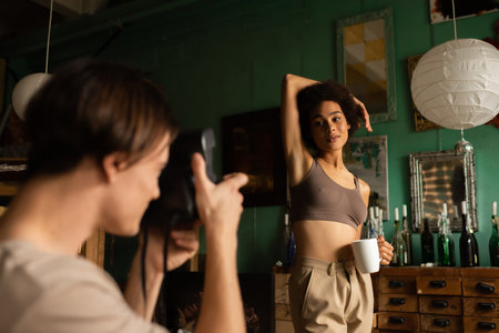 sexy african american woman in top posing near blurred boyfriend with vintage cameraの写真素材