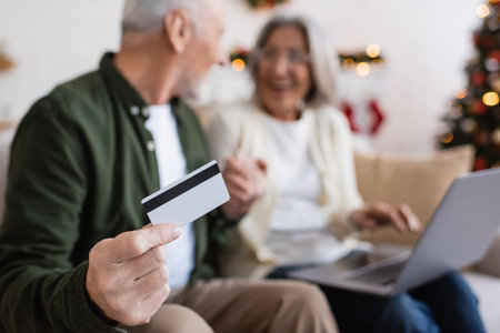 mature man holding credit card near wife with laptop while having online shopping on blurred backgroundの写真素材