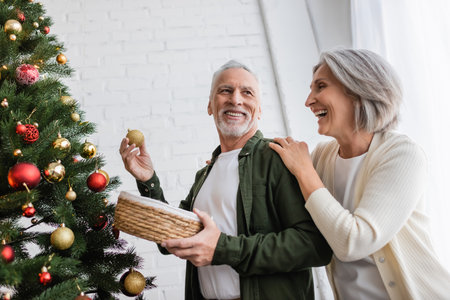 positive middle aged woman hugging husband decorating christmas treeの写真素材