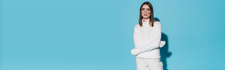 pretty young woman in trendy eyeglasses and white turtleneck posing with crossed arms on blue background, bannerの写真素材