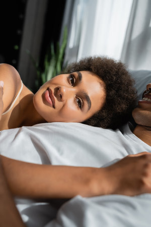 happy african american woman lying on bed near boyfriend and looking at cameraの写真素材