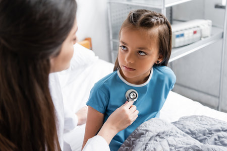 Burred doctor checking chest of patient with stethoscope in clinicの写真素材